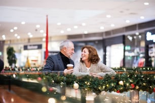 Senior couple doing Christmas shopping, drinking takeaway coffee. Shopping center at Christmas time.