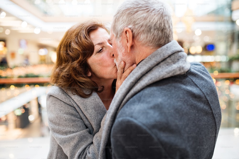 Senior couple doing Christmas shopping. Man and woman kissing. Shopping center at Christmas time.