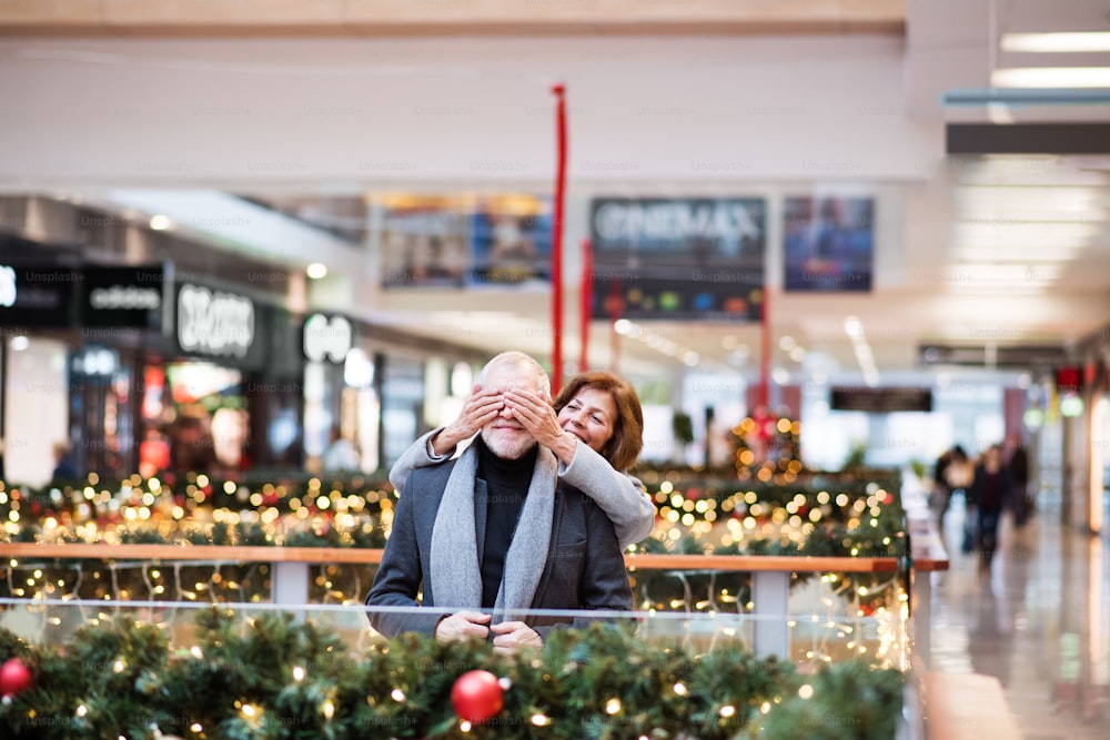 Senior couple doing Christmas shopping, having fun. Shopping center at Christmas time.