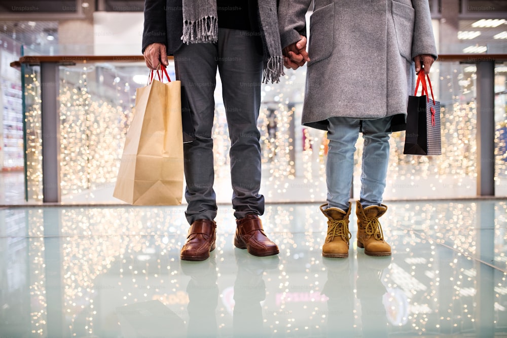 Unrecognizable senior couple doing Christmas shopping, holding hands. Shopping center at Christmas time.