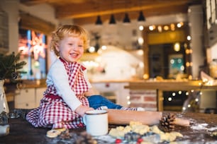 Garçon en bas âge faisant des biscuits au pain d’épices à la maison. Petit garçon assis sur la table. Période de Noël.