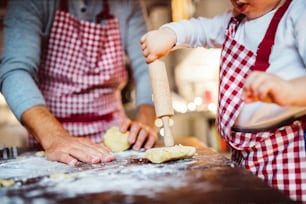 Hombre irreconocible y niño pequeño haciendo galletas en casa. Padre e hijo horneando galletas navideñas de pan de jengibre.