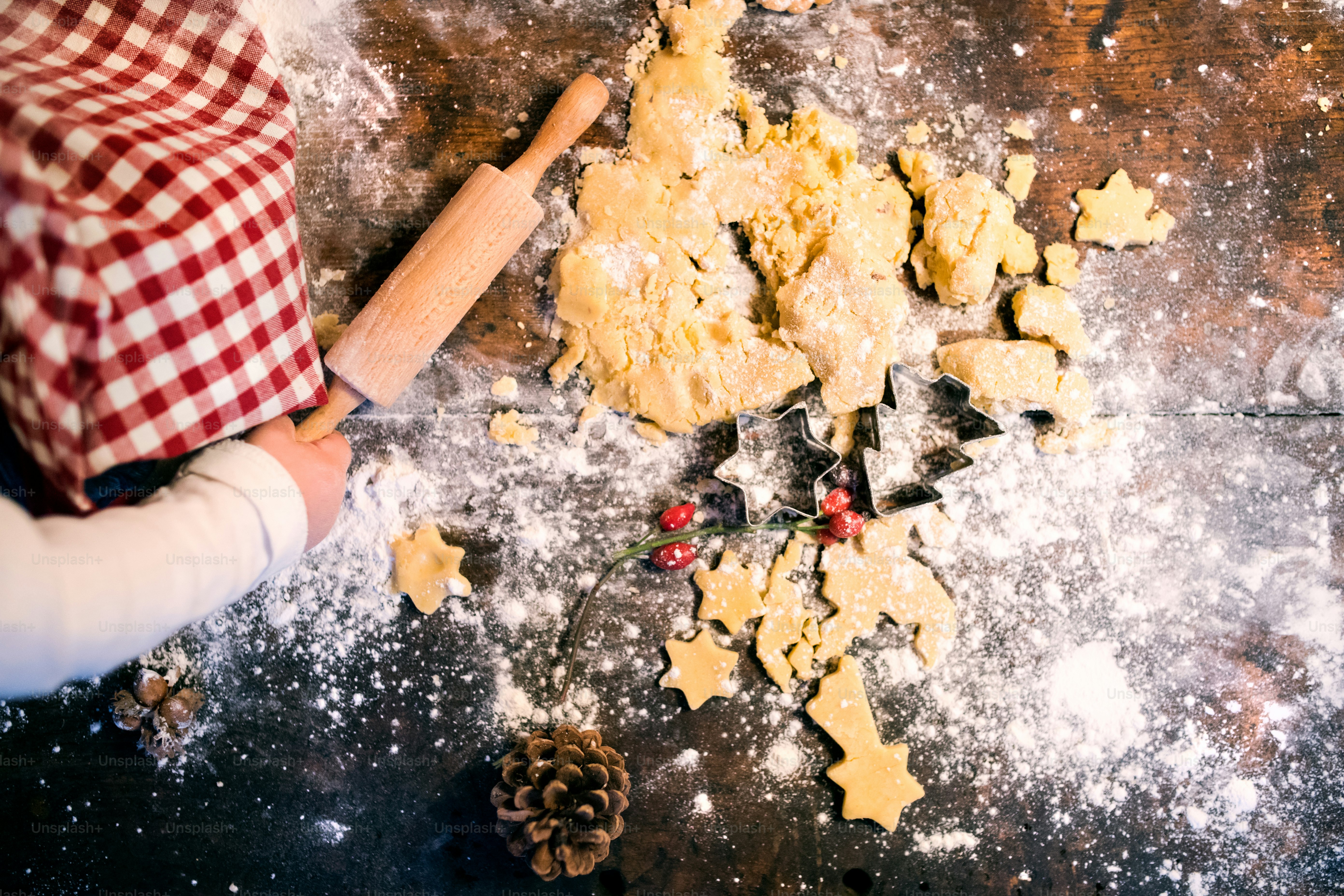 Balita yang tidak dikenali membuat kue jahe di rumah. Anak laki-laki kecil duduk di atas meja. Waktu Natal. Pemandangan udara.