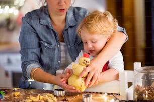 Femme méconnaissable et petit garçon faisant des biscuits à la maison. Mère et fils cuisant des biscuits de Noël en pain d’épice.