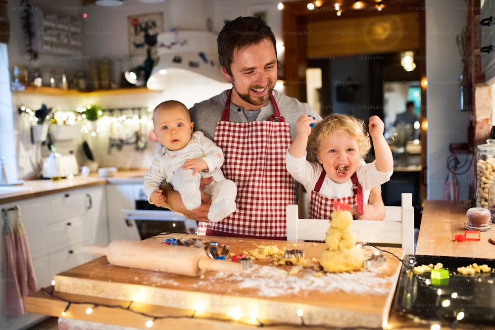 아기를 안고 있는 남자와 집에서 쿠키를 만드는 어린 소년. 아버지와 아들은 진저브레드 크리스마스 쿠키를 굽고 있다.