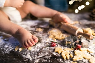 Young family making gingerbread cookies at home. Unrecognizable little baby sitting on the table. Christmas time.