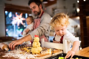 Hombre con un bebé y un niño pequeño haciendo galletas en casa. Padre e hijo horneando galletas navideñas de pan de jengibre.