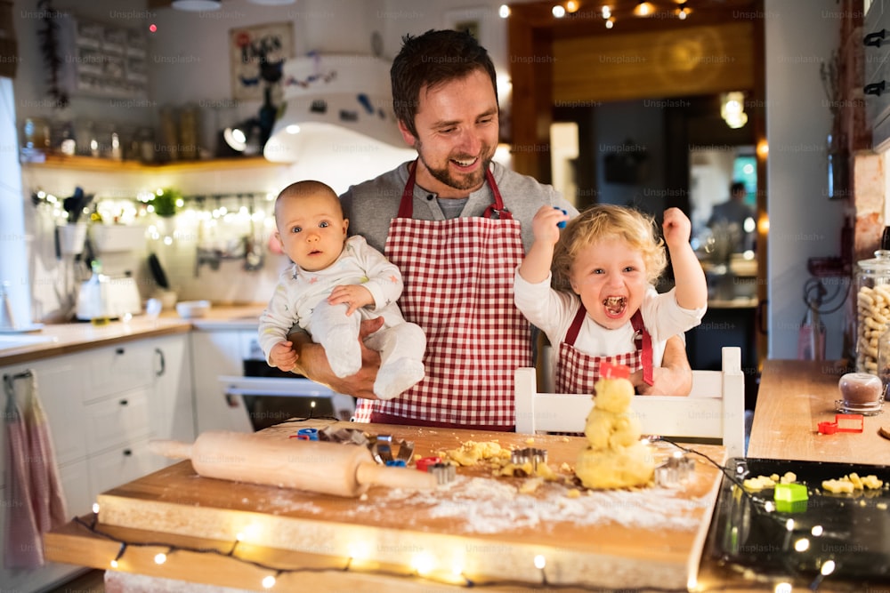 Man with a baby and a toddler boy making cookies at home. Father and son baking gingerbread Christmas cookies.