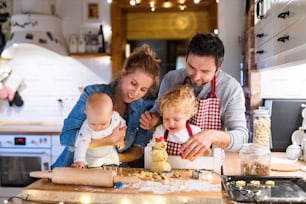 Hermosa familia joven haciendo galletas en casa. Padre, madre. niño pequeño y bebé divirtiéndose.
