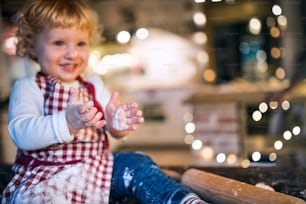 Toddler boy making gingerbread cookies at home. Little boy sitting on the table. Christmas time.