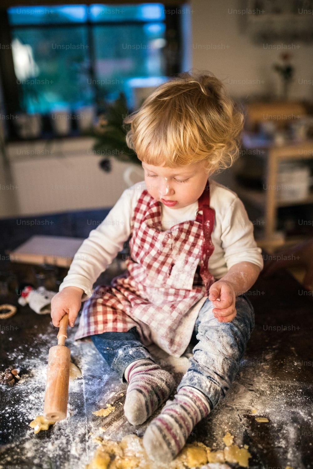 Toddler boy making gingerbread cookies at home. Little boy sitting on the table. Christmas time.