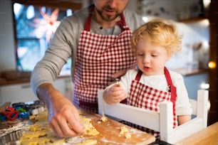 Hombre irreconocible y niño pequeño haciendo galletas en casa. Padre e hijo horneando galletas navideñas de pan de jengibre.