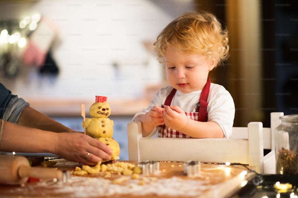 Toddler boy with unrecognizable mother making gingerbread cookies at home. Christmas time.