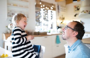 Cute little girl in striped dress with her father in the kitchen having fun, lauging. Christmas season.