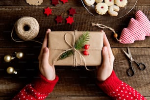 Hands of unrecognizable woman wrapping and decorating Christmas present laid on a wooden table background. Studio shot.