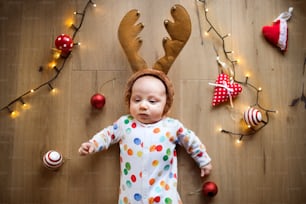 Little baby boy lying on the floor wearing reindeer headband at Christmas time. High angle view.
