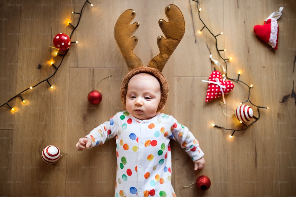 Little baby boy lying on the floor wearing reindeer headband at Christmas time. High angle view.