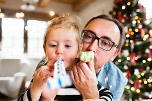 Giovane padre con la piccola figlia carina al periodo natalizio che soffia fischietti di festa.
