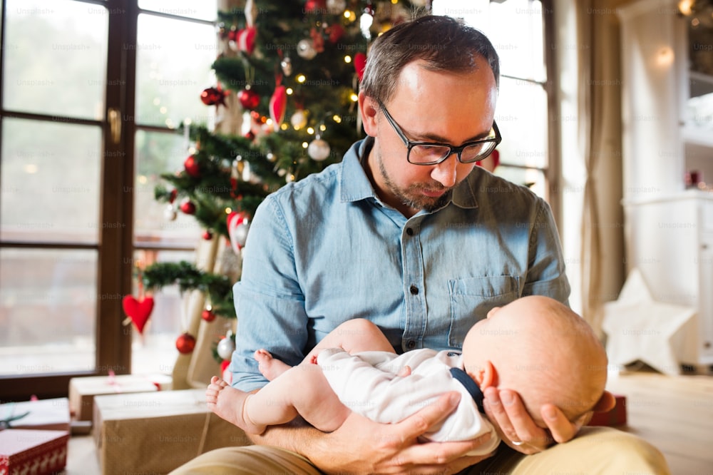 Young father with baby son in front of Christmas tree. Man holding a baby in his arms.