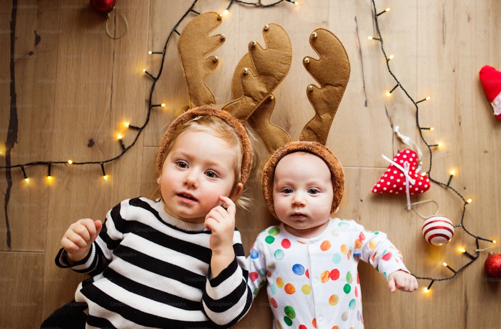 Little boy and girl lying on the floor at Christmas time. Siblings wearing reindeer headbands. High angle view.