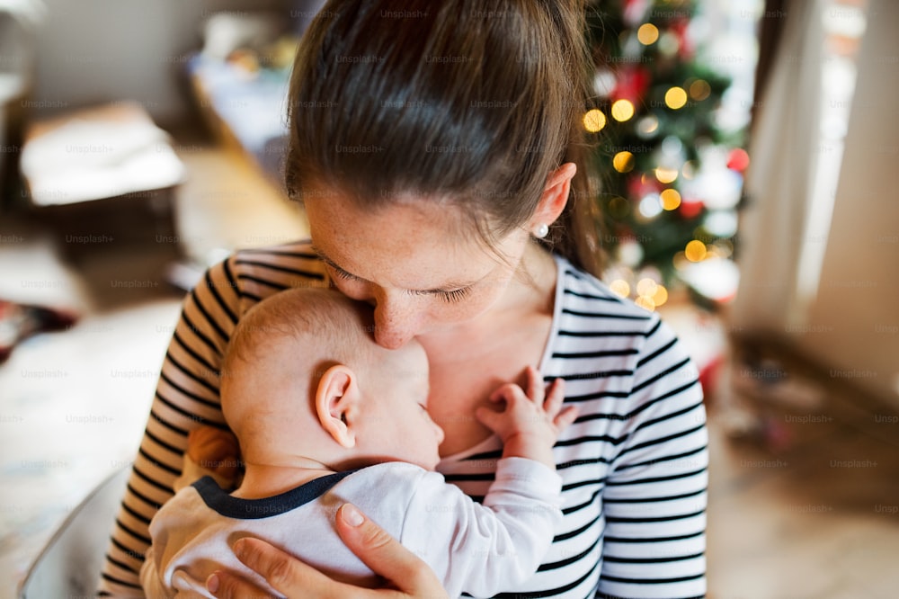 Hermosa joven sosteniendo a un bebé en sus brazos en Navidad.