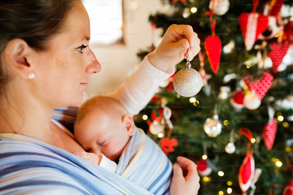 집에서 아기를 안고 크리스마스 트리를 장식하는 젊은 여자.