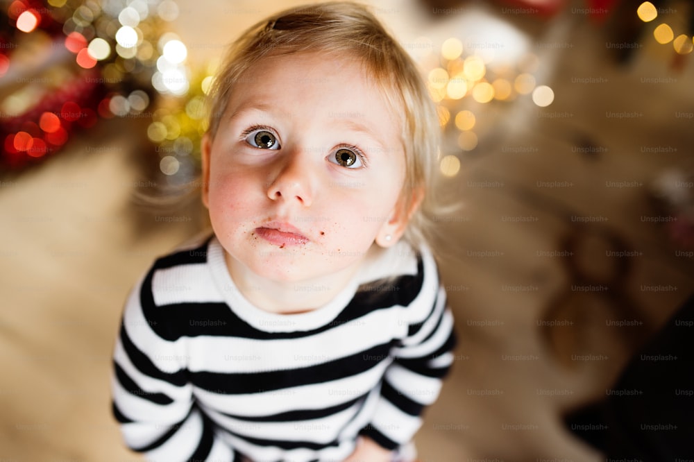 Bambina carina in vestito a righe, briciole intorno alla bocca. Periodo natalizio.