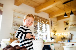 Cute little blond girl in striped dress sitting on kitchen table. Christmas season.