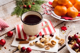 クリスマスの作曲。コーヒーのカップ、ドライフルーツ、クランベリーとナッツ、プレート上のみかんのボウル。テーブルの上に置かれたさまざまなオブジェクト。木の背景にスタジオショット。