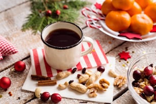 Christmas composition. Cup of coffe, bowl with dried fruit, cranberries and nuts, tangerines on plate. Various objects laid on table. Studio shot, wooden background.