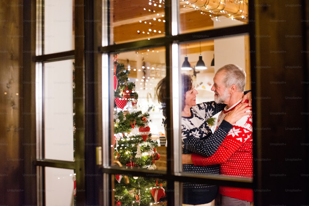 Hermosa pareja mayor en suéteres de lana con patrón nordinc en Navidad. Disparado a través del vidrio.