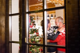 Lindo casal sênior em suéteres de lã com padrão nordinc na época do Natal. Tiro através do vidro.