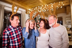 Senior friends wearing reindeer antlers headbands at Christmas time, having fun.