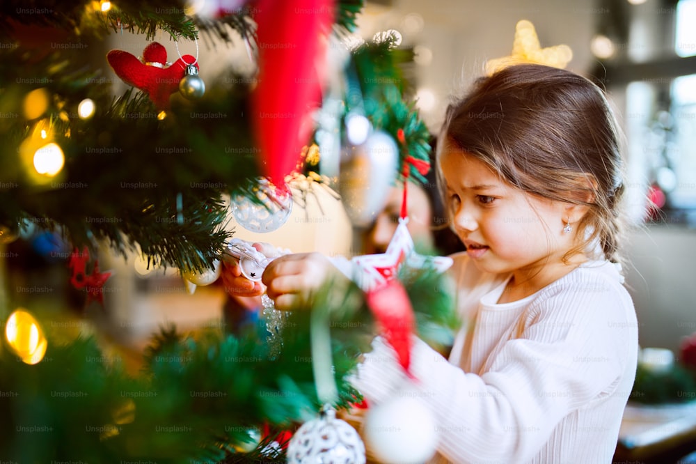 Beautiful small girl decorating Christmas tree at home.