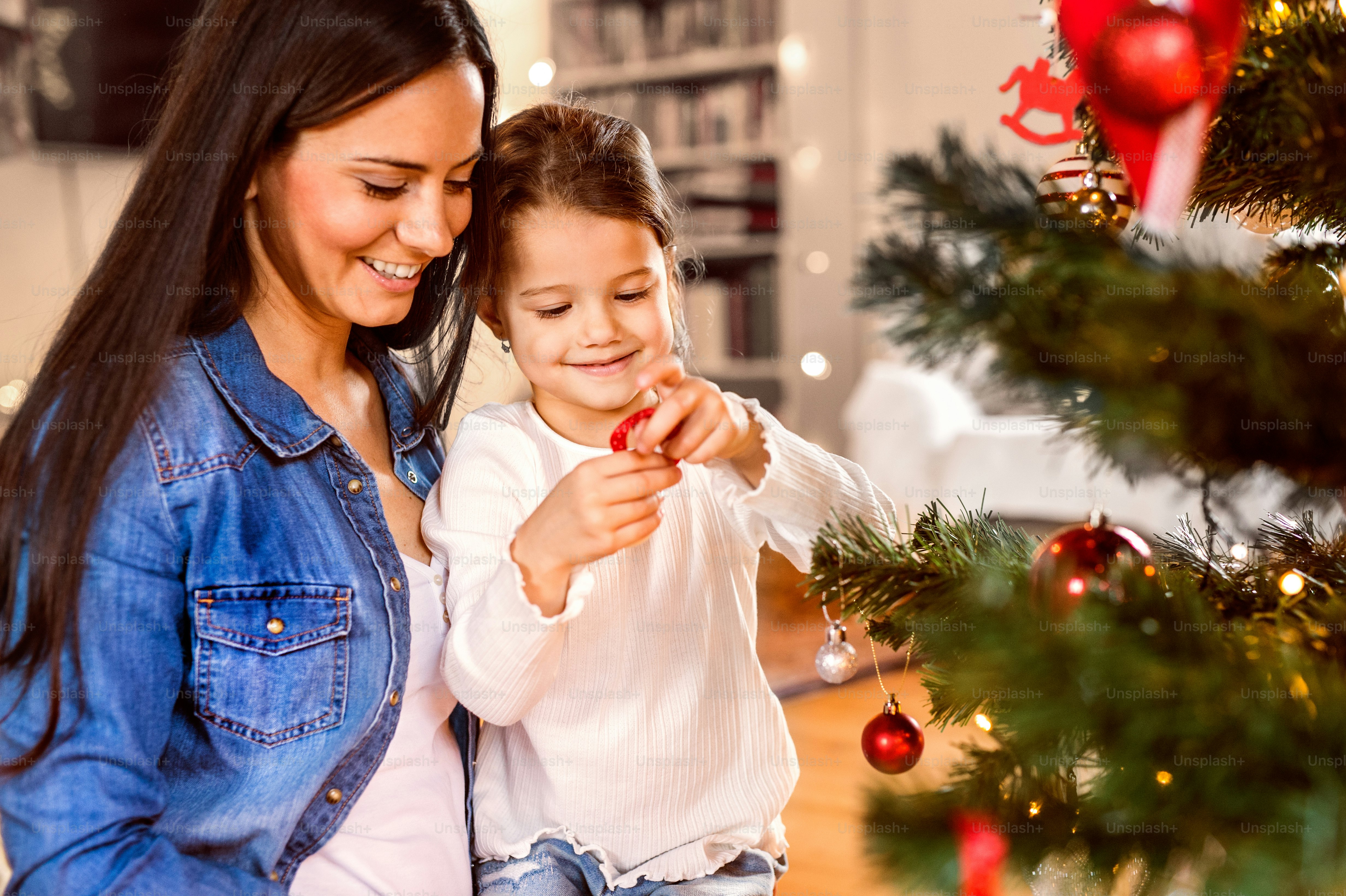La joven madre con su pequeña hija en casa decorando juntos el árbol de ...