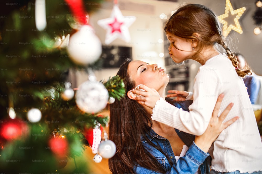 Young mother with his little daughter at home decorating Christmas tree together.
