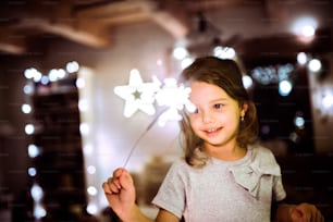 Beautiful little girl with a sparkler at Christmas time at home.