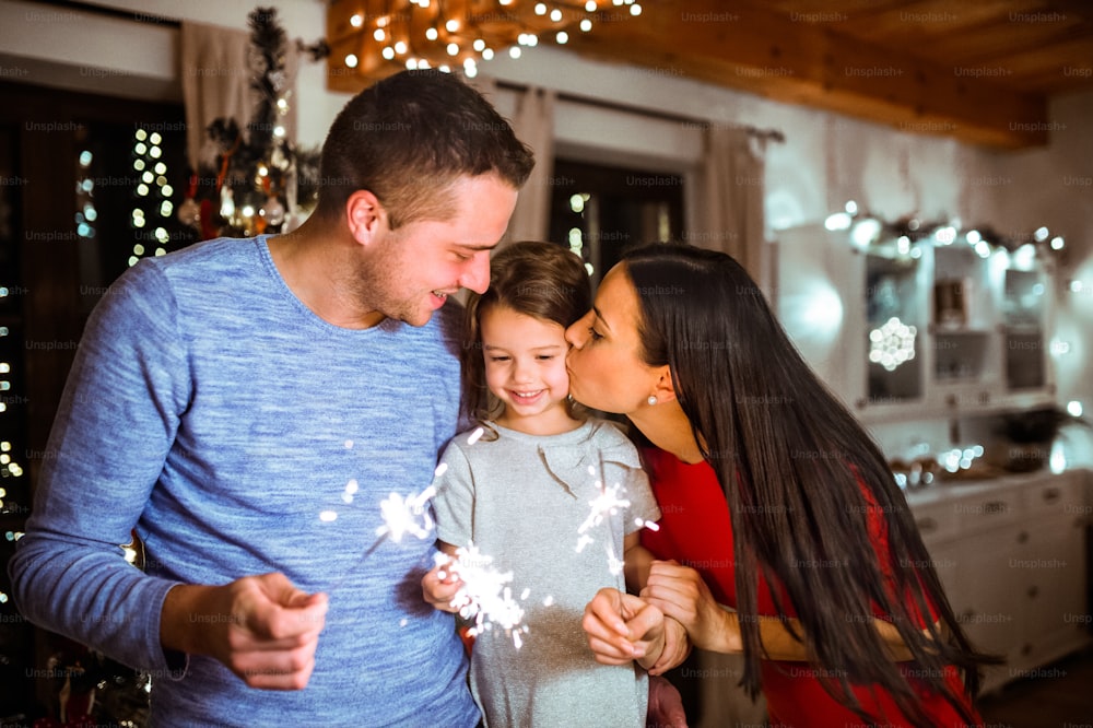 Beautiful young family with little daughter with sparklers at Christmas time at home.