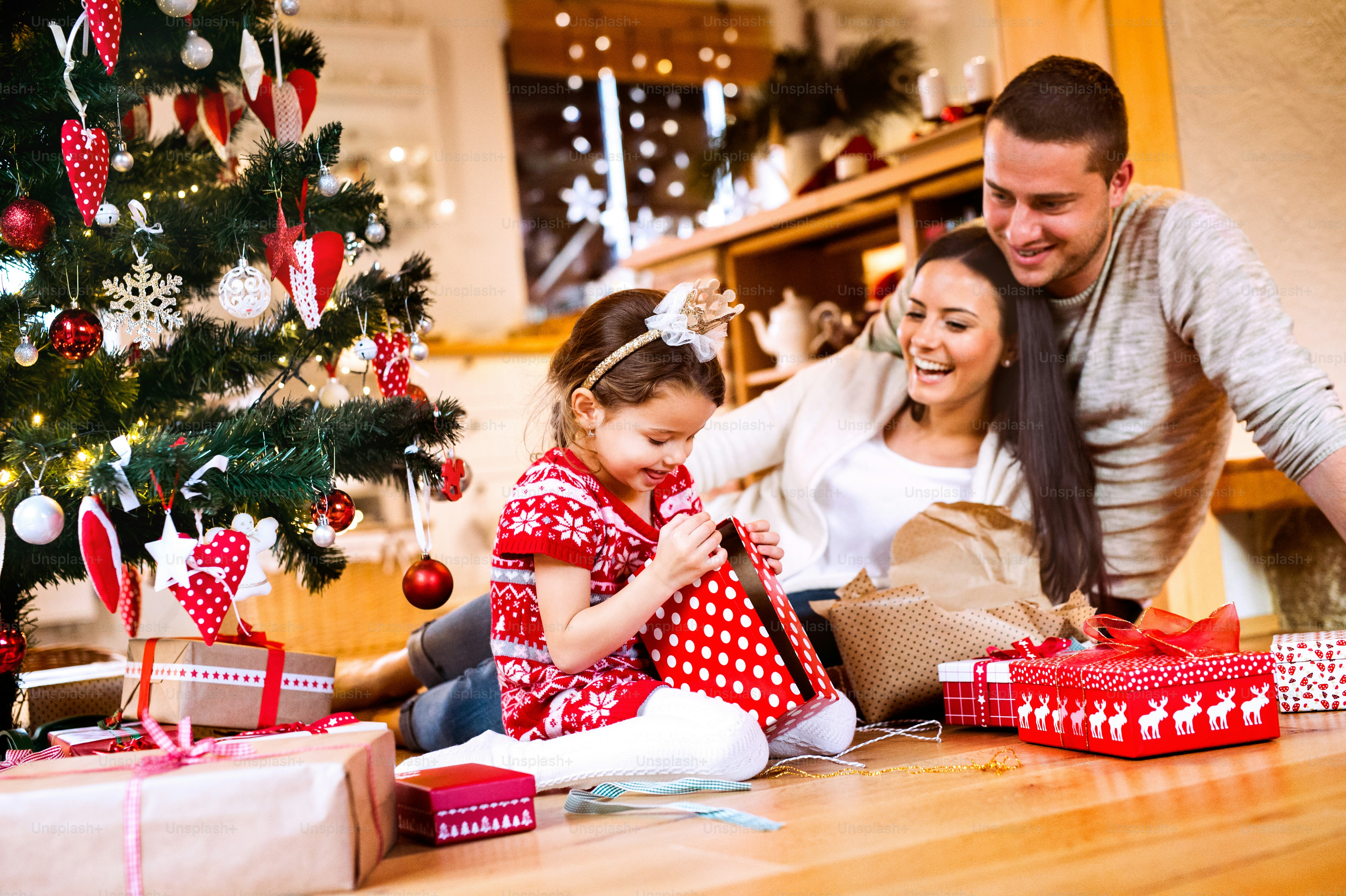 Hermosa familia joven con hija pequeña en el árbol de Navidad en casa desempacando regalos.