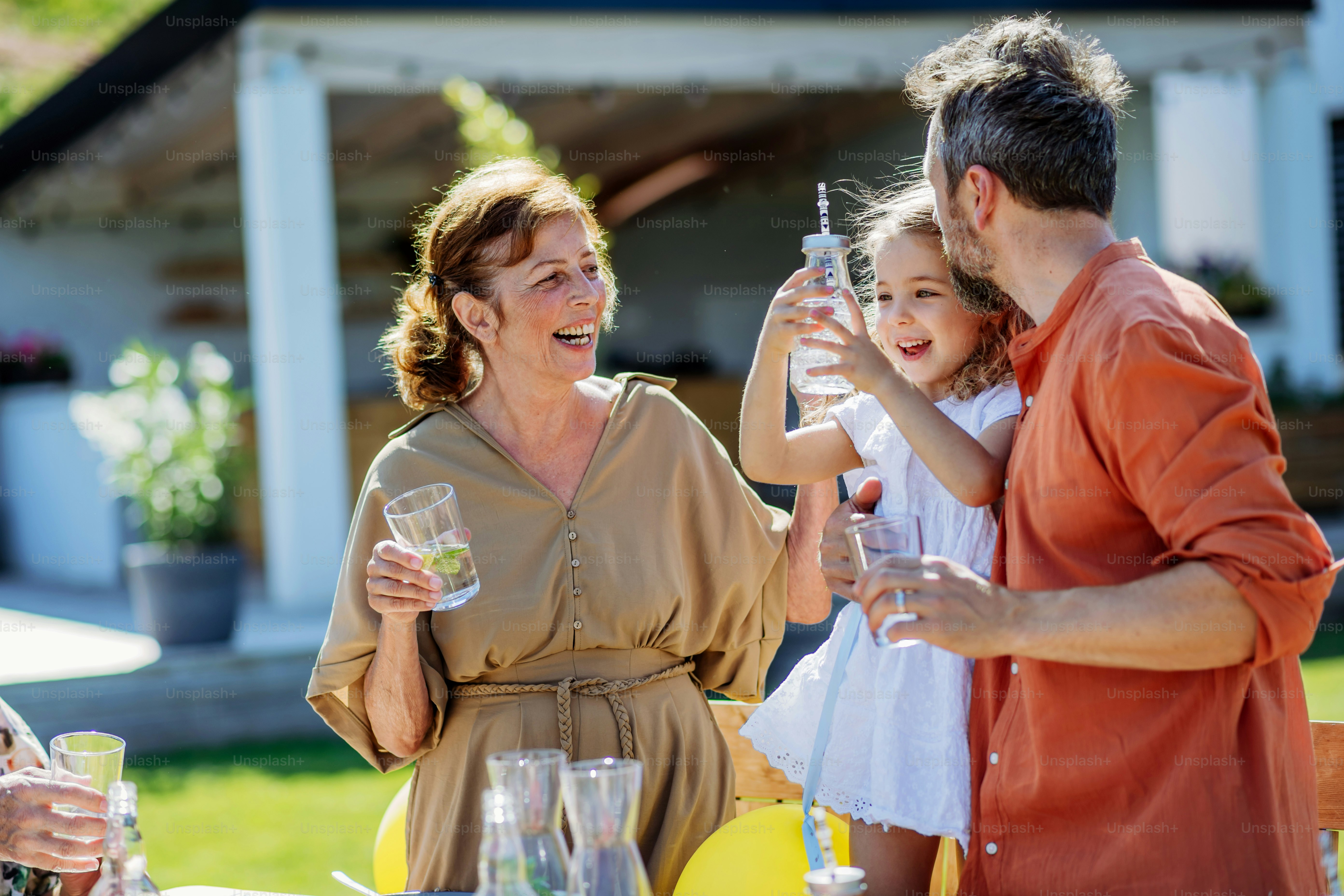 Multi generation family having garden party celebration, little girl with her dad and grandmother drinking a water with lemon, having nice time