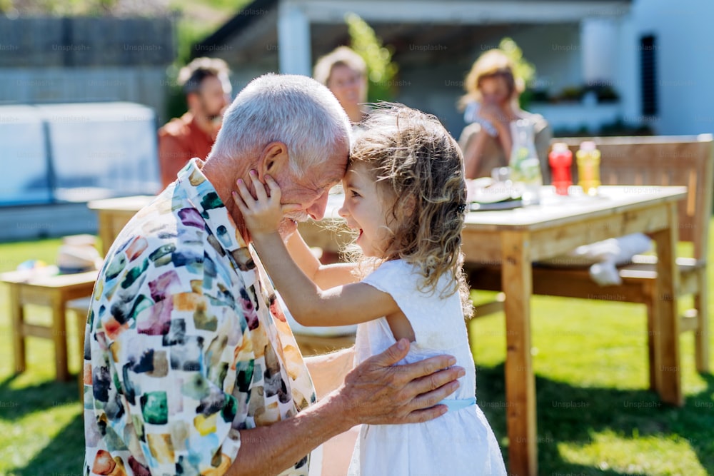 Happy little girl embracing her grandfather at generation family birthday party in a summer garden.