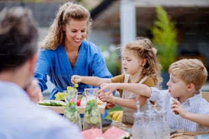 Eine Familie, die eine Gartenparty feiert, Kinder essen Snacks, lachen und haben Spaß.