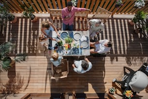 Une vue de dessus de 3 générations de famille mangeant au dîner de barbecue sur le patio, les gens assis sur le patio avec grill.