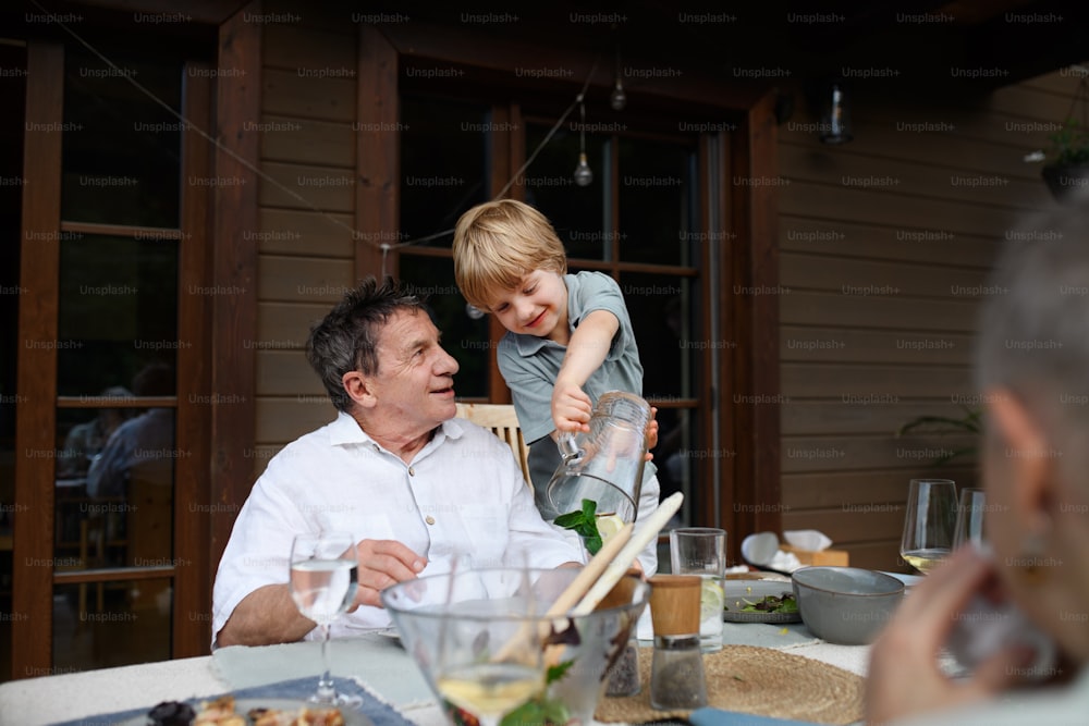 パティオで家族のお祝いをしているときに祖父にレモネードを注ぐ小さな男の子。