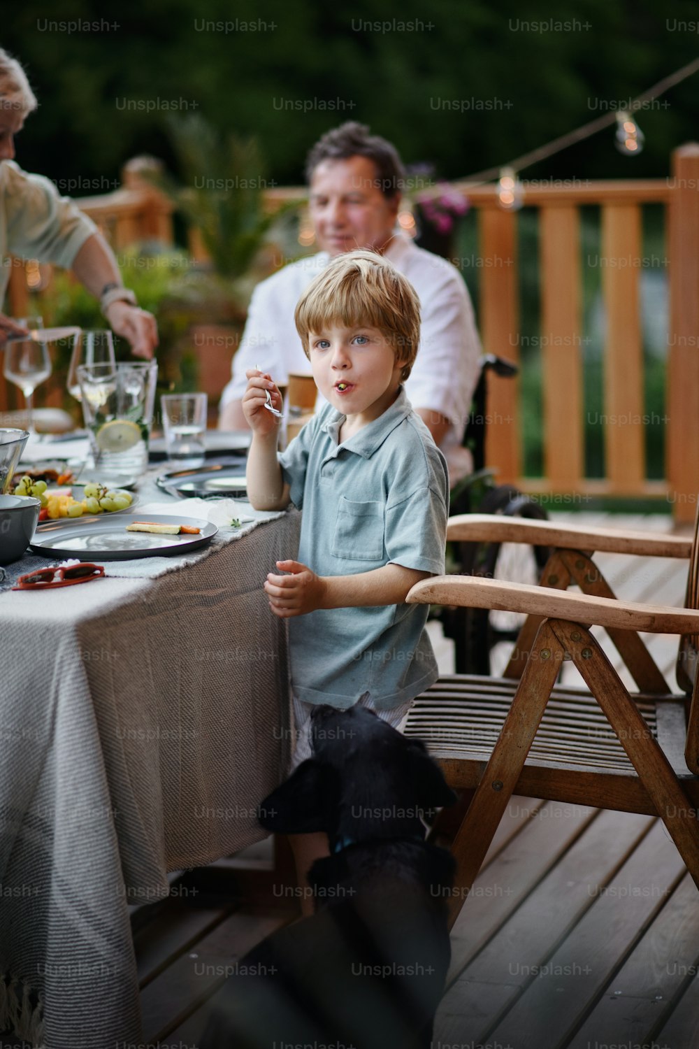 パティオでバーベキューパーティーのディナーを食べる家族、野菜をグリルして楽しんでいる小さな男の子。