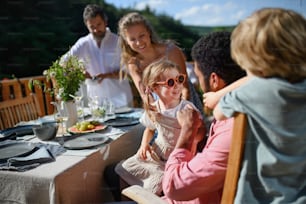 Una familia con niños divirtiéndose en la cena de barbacoa en el patio, gente sentada a la mesa en el patio y hablando