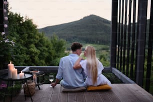 Una giovane coppia che riposa all'aperto sulla terrazza della piccola casa nel bosco con vista la sera, il fine settimana in una piccola casa in campagna, vita sostenibile.