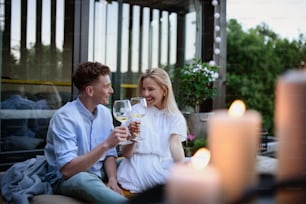 Una pareja joven tintineando con vino al aire libre, fin de semana en una pequeña casa en el campo, vida sostenible.