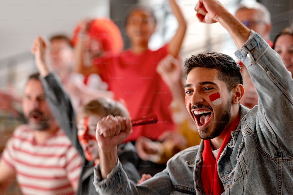 Excited football fans supproting an Austrian national team in live soccer match at stadium.