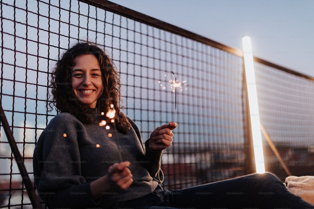 A young woman with sparklers having fun at rooftop in the city, close up.